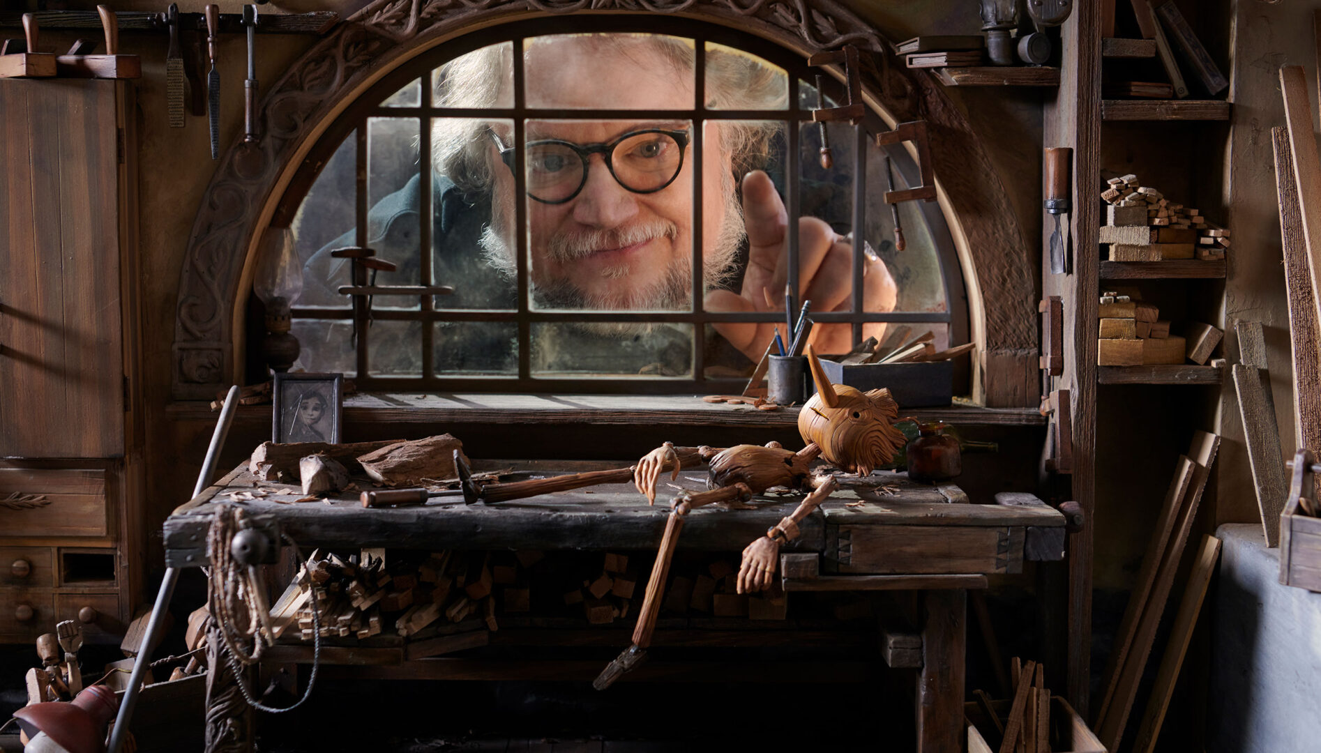Photo of a man looking through a window towards a Pinocchio puppet laying on a table