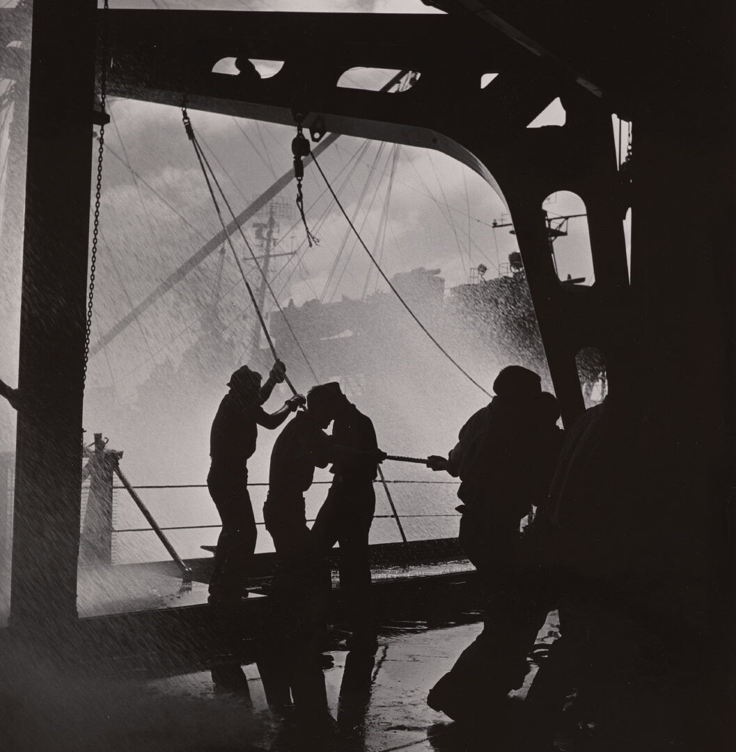 Black and white photograph of people in shadow on a boat with water coming on board