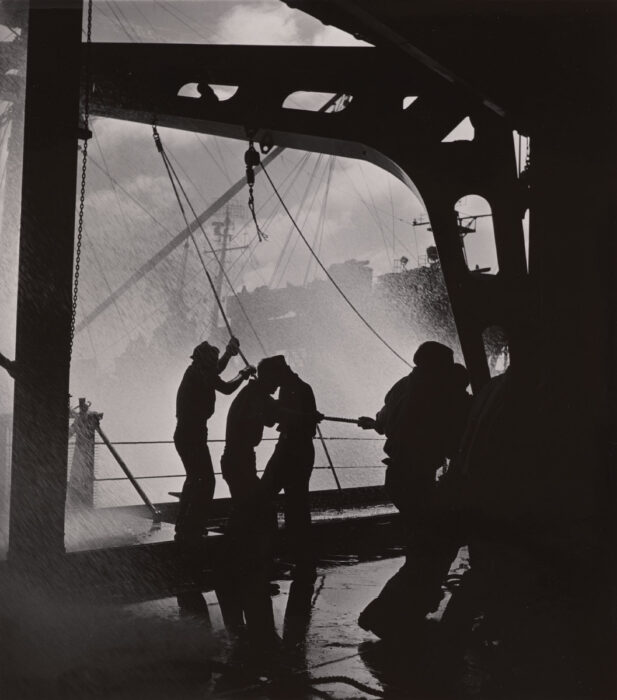 Black and white photograph of people in shadow on a boat with water coming on board