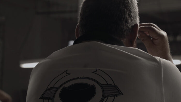 Black and white film still of the back of someone's head and the top of their back