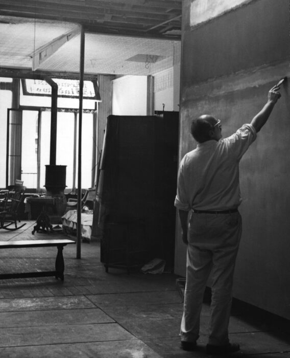 A person painting on a large canvas in a studio.