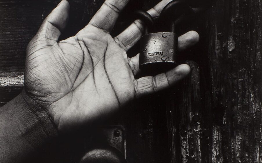 Black and white photo of a hand holding a lock in front of a wooden door