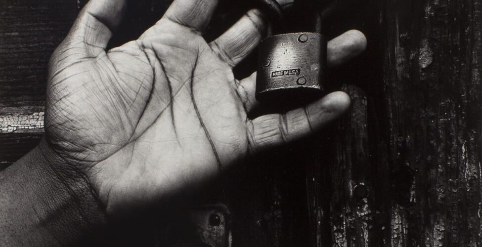 Black and white photo of a hand holding a lock in front of a wooden door