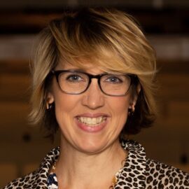 Color photograph of a woman with blonde hair wearing glasses and smiling