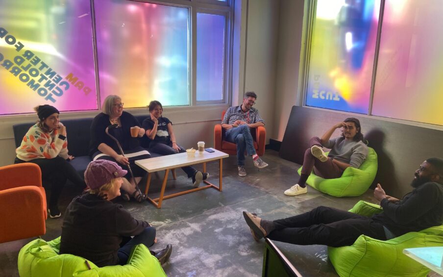 Seven people sitting in a circle on couches and bean bags in the lobby of the PAM CUT building