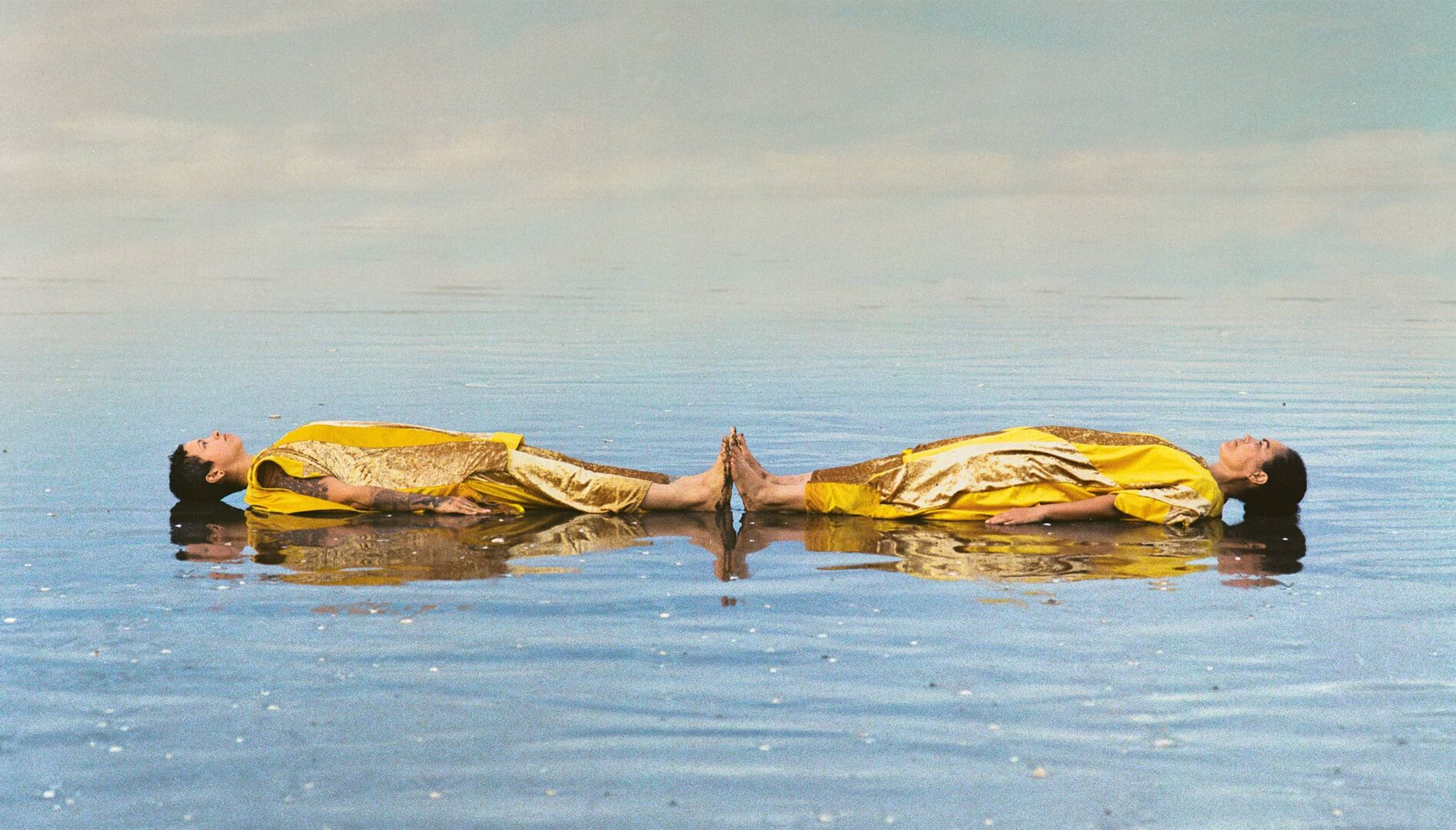 Two people in gold gowns floating on top of water.