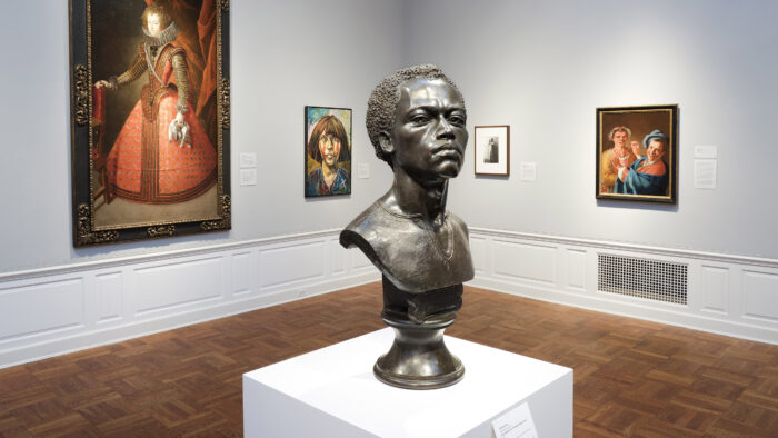 Installation shot with a sculpture in the foreground and art hanging on the walls behind.