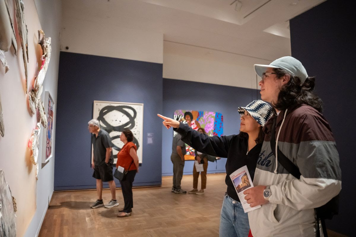 Photo of two people in a gallery. One is pointing at an artwork.