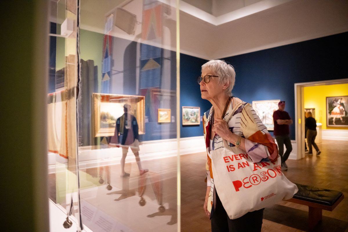 Photo of a woman with short white hair looking at an artwork in a gallery