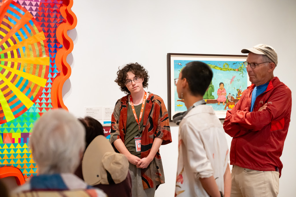 Photo of a group of people standing and talking around an artwork.