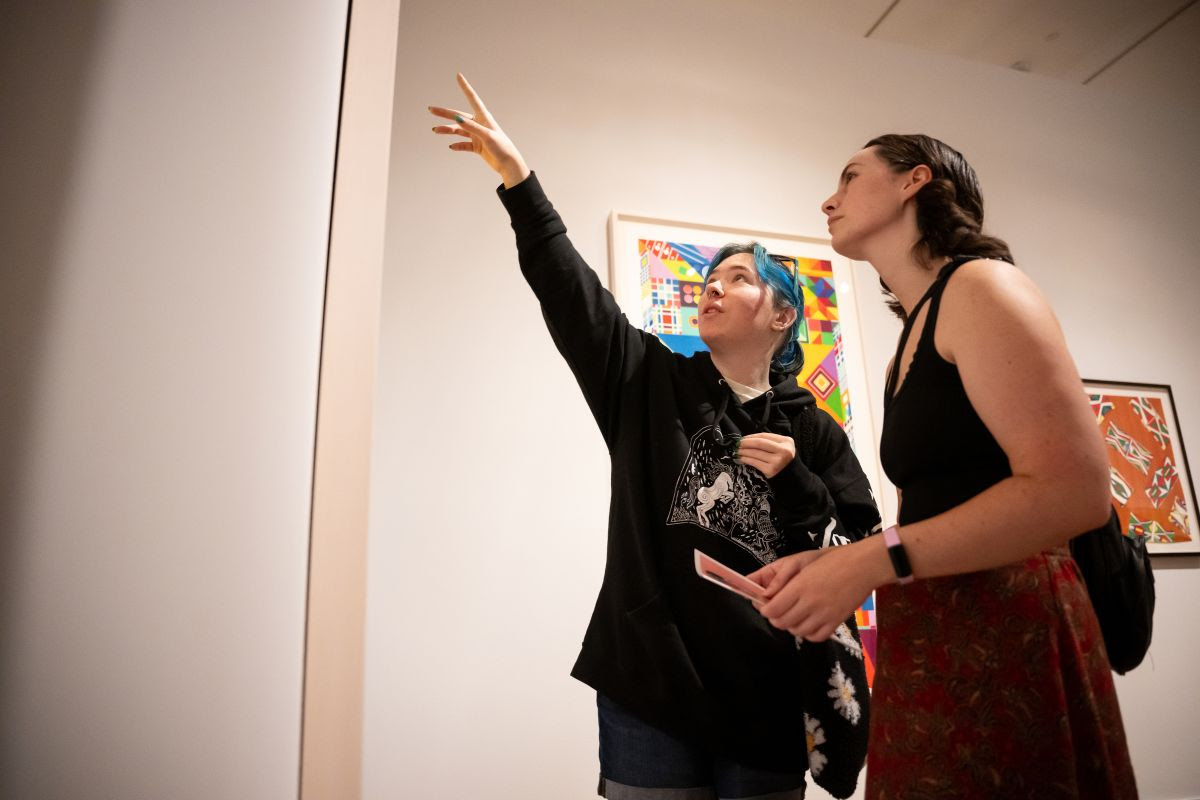 Photo of two people looking at an artwork. One of them is pointing upwards.