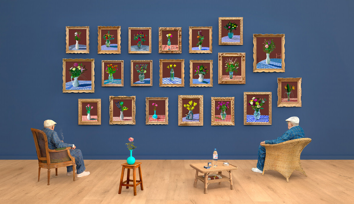 A blue gallery wall with a grid of framed art on it. Looking towards the wall are two chairs and two tables. David Hockney sits in the lefthand chair.