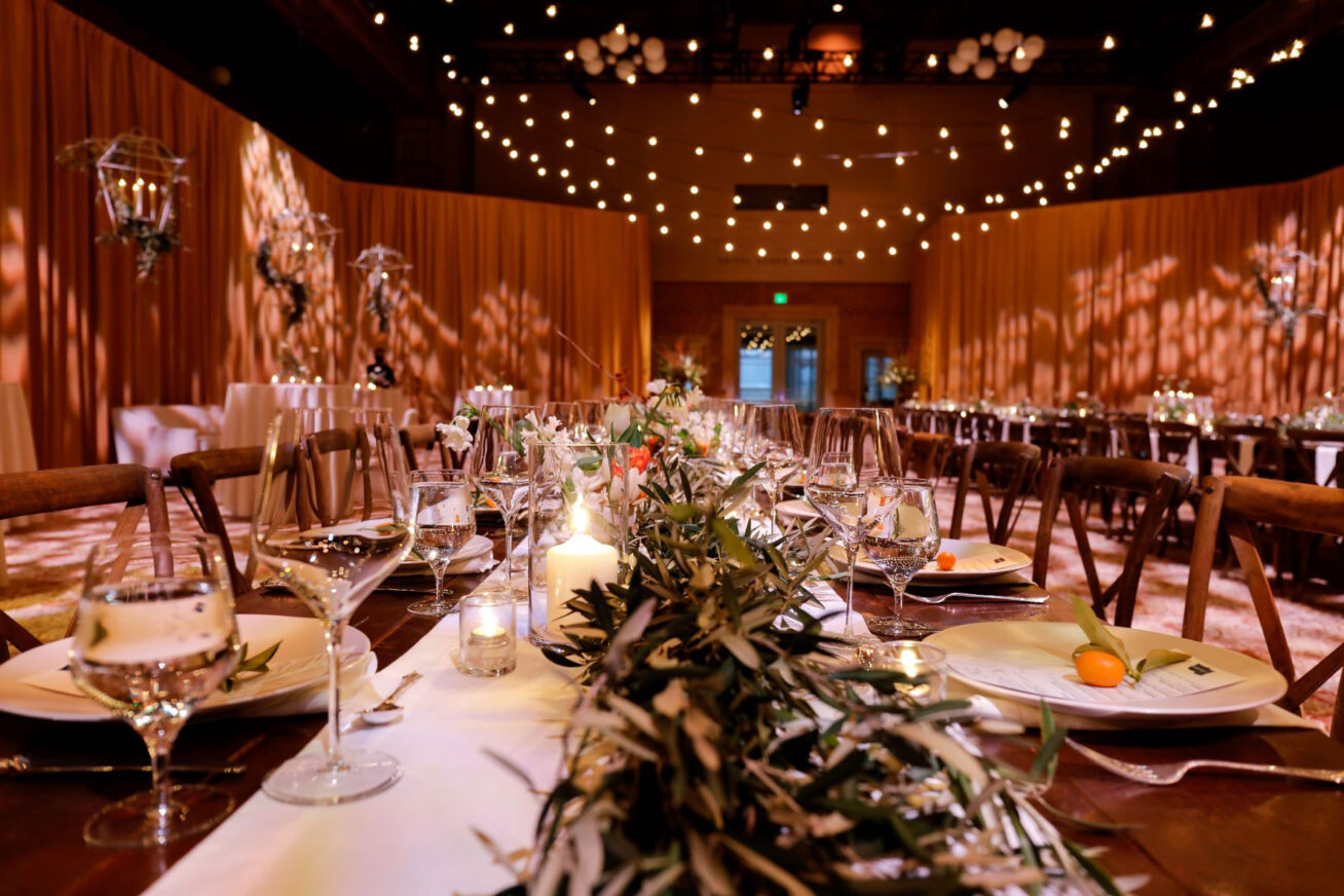 Photograph of a long table set with wine glasses, plates, and silverware