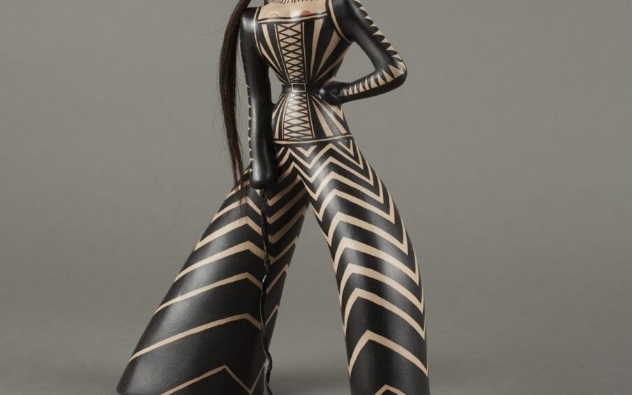 Stylized figure adorned with black-and-white triangular patterns. Details include reddish circular earrings similar to the shape of the lips, a long ponytail, and whip.