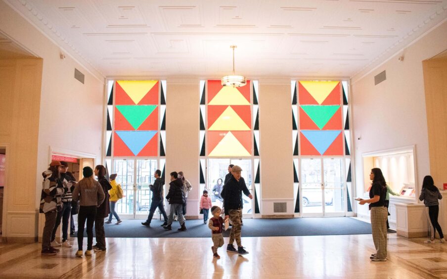 Lobby entrance of Portland Art Museum from Park Avenue. A bright space with three glass doors, full of visitors.