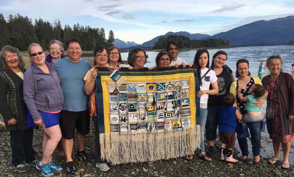 Photograph of a group of female weavers standing on a beach holding up a woven artwork